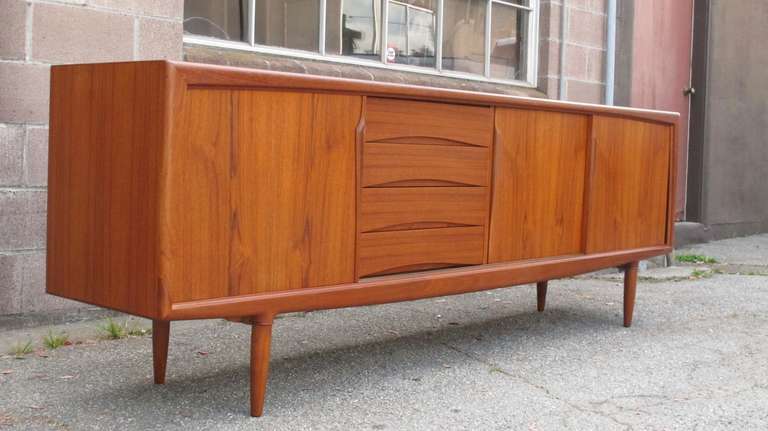 Danish modern teak credenza designed by by Gunni Oman for Axel Christiansen. Features sliding doors with sculpted pulls and adjustable shelves, series of four drawers in center. Raised on round tapered legs. Excellent condition.
