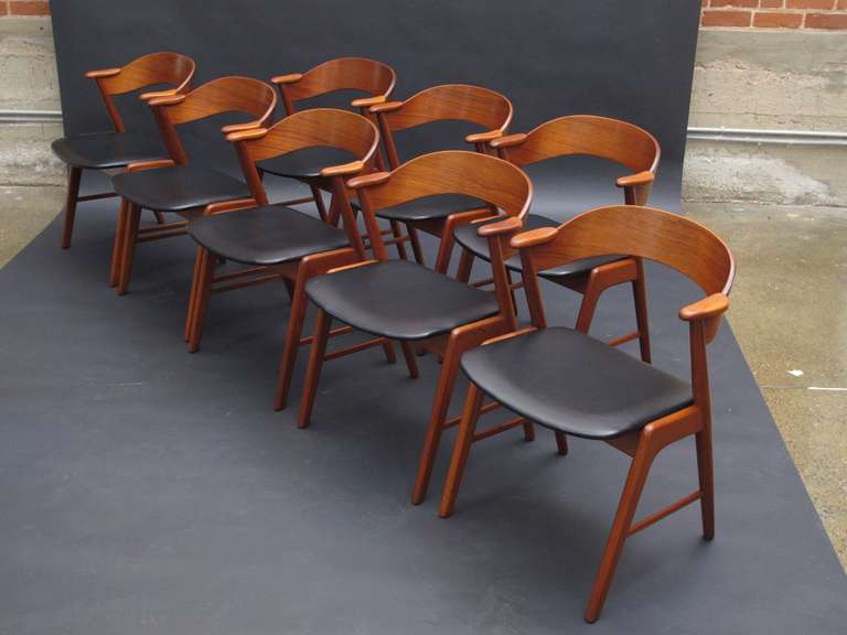 Set of eight teak dining chairs designed by Kai Kristiansen. The chairs are made of solid teak wood frame with bent ply back rest and unique arm rest. Seats upholstered in original vinyl. Two additional chairs available at $675 each, for set/10.
