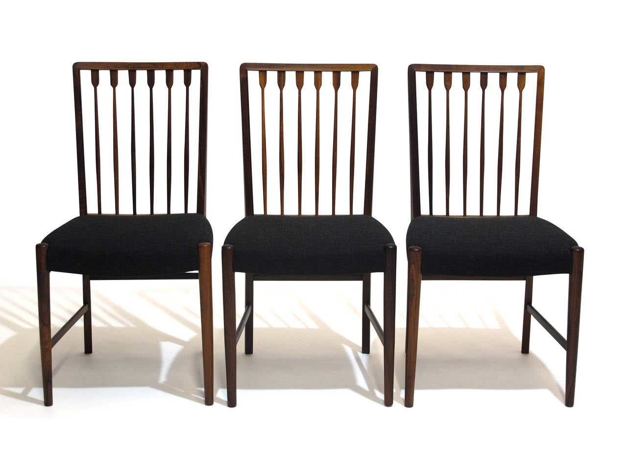 Elegant rosewood dining chairs by master cabinetmaker Georg Kofoed, circa 1938. Solid rosewood with hand carved sculpted spindles on back rest, round tapered legs with cross stretchers. Newly upholstered in a dark grey wool textile; over the