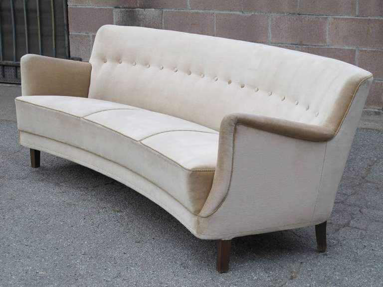 1935 elegant curved sofa with button tufted back and sculpted arms features an impressively constructed frame with double layers of springs in the seat. Original beige mohair fabric in excellent condition. Raised on dark walnut stained tapered legs.