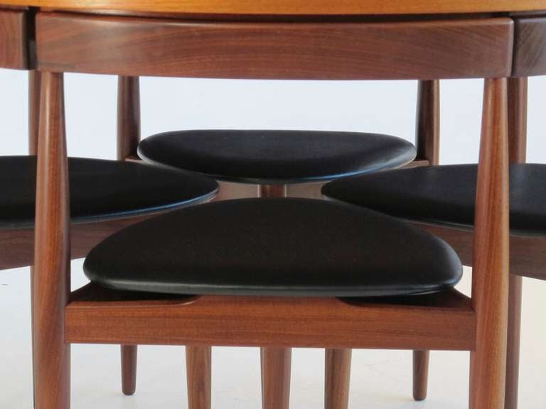 Danish designed teak dining set by Hans Olsen for Frem Rojle, Denmark 1962. Round table with four three-legged chairs covered in original black vinyl. The backs of the chairs integrate into the apron of the table creating this functional work of art.