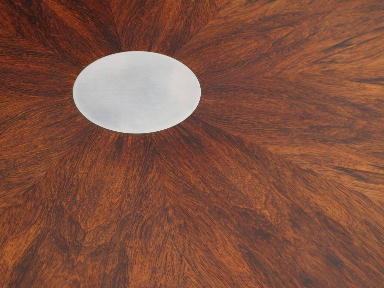 Mid-Century Danish dining table designed by Steen Ostergaard for Poul Cadovius. Stunning Brazilian rosewood arranged in a bookmatched star pattern around an aluminum disc in center, with silver aluminum trim on outer edge, on a polished pedestal