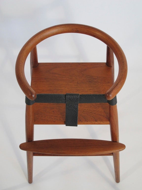 Teak highchair designed by Nanna Ditzel. Teak with curved back and leather straps. Adjustable foot rest.