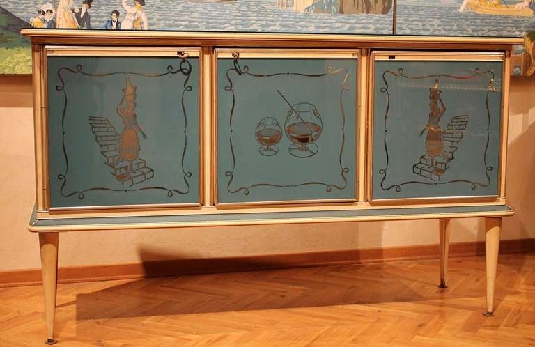 Italy, 1950's
Early 1950's petrol blue three doors cabinet created by Umberto Mascagni of Bologna, Italy. Reverse painted glass door fronts, two doors featuring a woman walking down the stairs, the central door depicting a glass of liquor. This