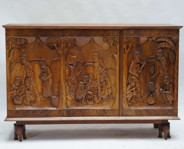 Armoire en bois ethnique unique en son genre, datant des années 1950 et représentant la vie rurale au Zaïre (aujourd'hui le Congo). Technique du bas-relief sur bois massif. Excellent état d'origine. Les pieds avant de ce meuble ont été façonnés en