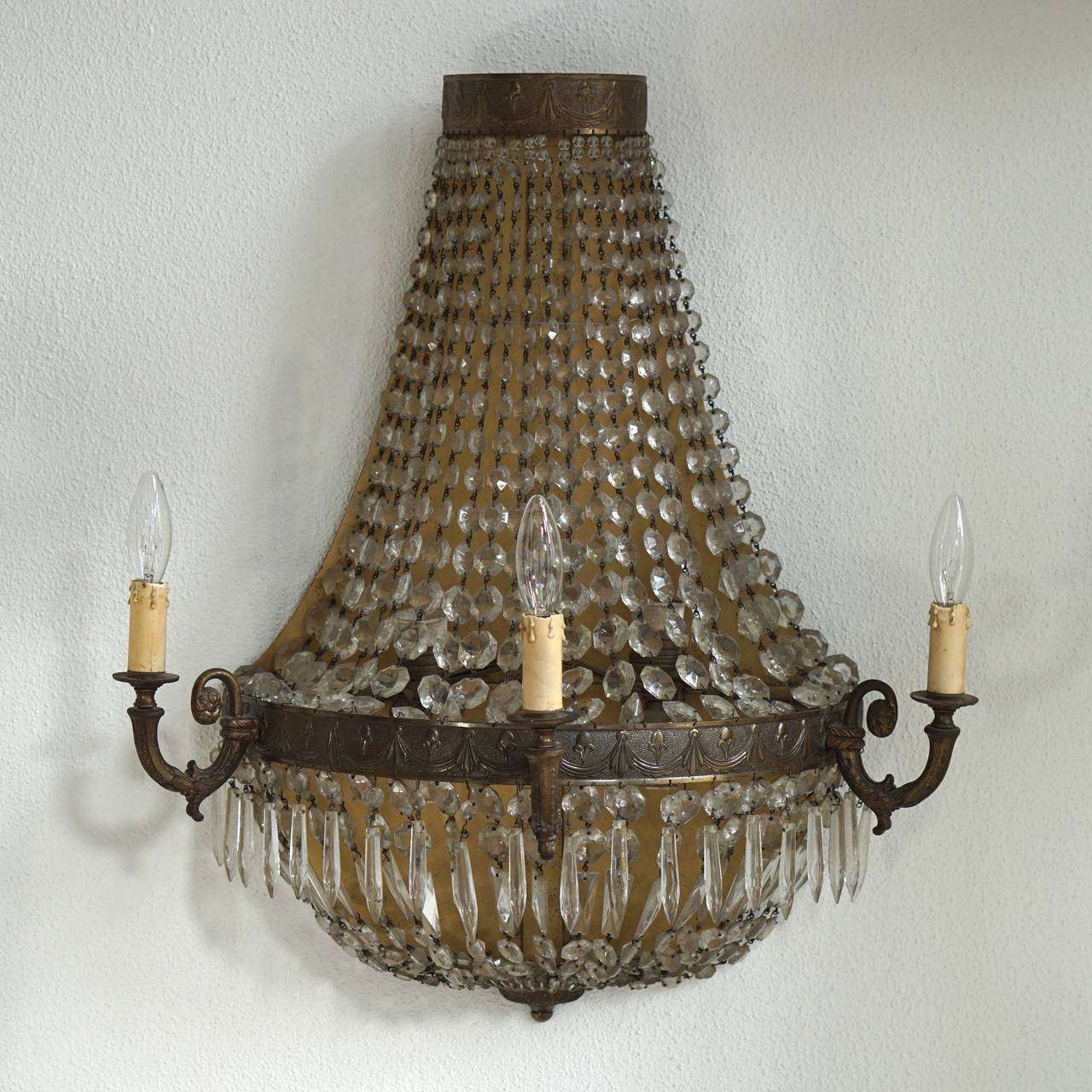 Set of four large French bronze and crystal three-arm wall sconces with decorative bead work, cascading prisms and original crystal bobaches. Originally candle powered and has been electrified, mid-20th century.