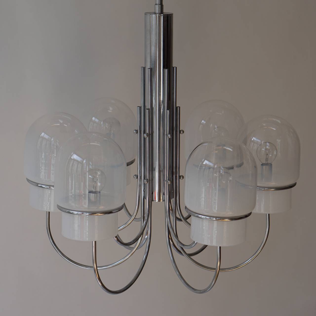 Italian six arched arm chrome and milk glass chandelier, circa 1960s. 
A single reeded stem issuing six scrolled arms with rounded milk glass shades. 

Diameter 60 cm.
Height 110 cm.