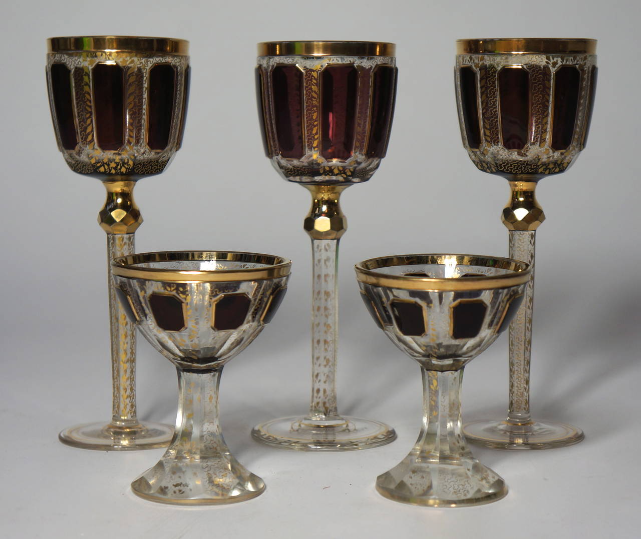 A fine and rare collection of late 19th century Moser cut crystal glasses comprising:

Three amethyst coloured cabochon stemmed wine glasses, covered overall with gilt leaves and curls and gilt rim
Nine red colored cabochon medieval style calice