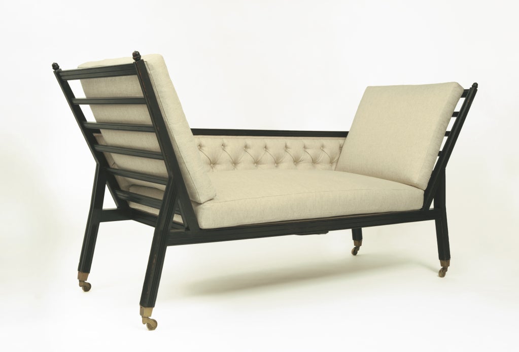 Ebonized wood with reeded decoration and acorn finials, fitted brass sabot castors. Tufted upholstered back, loose seat and arm cushions.

This unusual settee appropriates the basic shape of the so-called “Knole” sofa – made popular by an