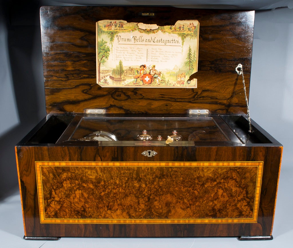 This is a fabulous 19th Century Swiss 12 air musical box, the hinged marquetry lid opening to reveal a 13 inch cylinder with central drum, 5 bells in sight, a snare drum and a castagnette and the original pictorial tune card to the lid. Circa 188o