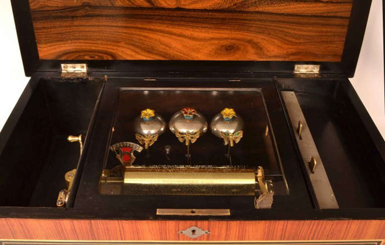 This is a lovely antique Swiss 10 air rosewood cylinder bells-in-view music box, circa 1880 in date. The movement is stamped BHA which stands for Barnett Henry Abrahams. 

The rosewood case is decorated with marquetry of musical instruments and is