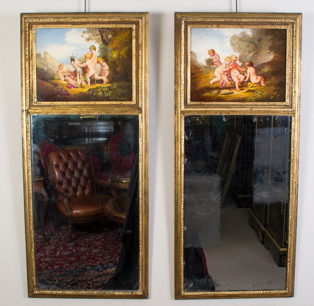 This is an antique pair of highly decorative French giltwood trumeau mirrors, circa 1920. 

Each has a rectangular mirror below a hand painted scene of playful cherubs in the manner of Boucher. 

The quality and craftsmanship of these stunning