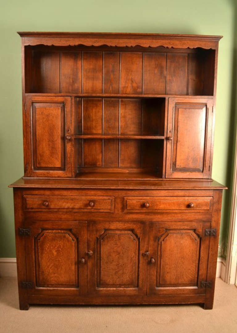This very decorative antique English dresser was made from solid oak and dates from around 1900.

The top has a pair of small panelled cupboard doors on either side with an open rack in the centre for displaying your plates, the bottom has two