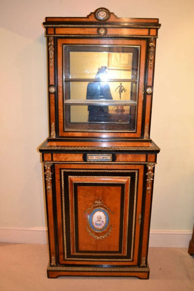 This is a gorgeous antique French porcelain and gilded ormolu mounted, brass inlaid, satinwood and ebonised display cabinet c.1860 in date.

The smaller hand painted Sevres porcelain plaques have floral motifs, the large oval plaque depicts a bust