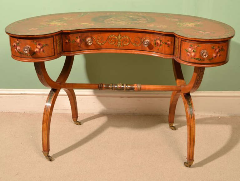 This is an exquisite antique Sheraton Revival satinwood and polychrome decorated kidney shaped dressing table, c.1890 in date.

The top is hand painted with a central panel of a musician playing to a group of people with ribbon tied swags of