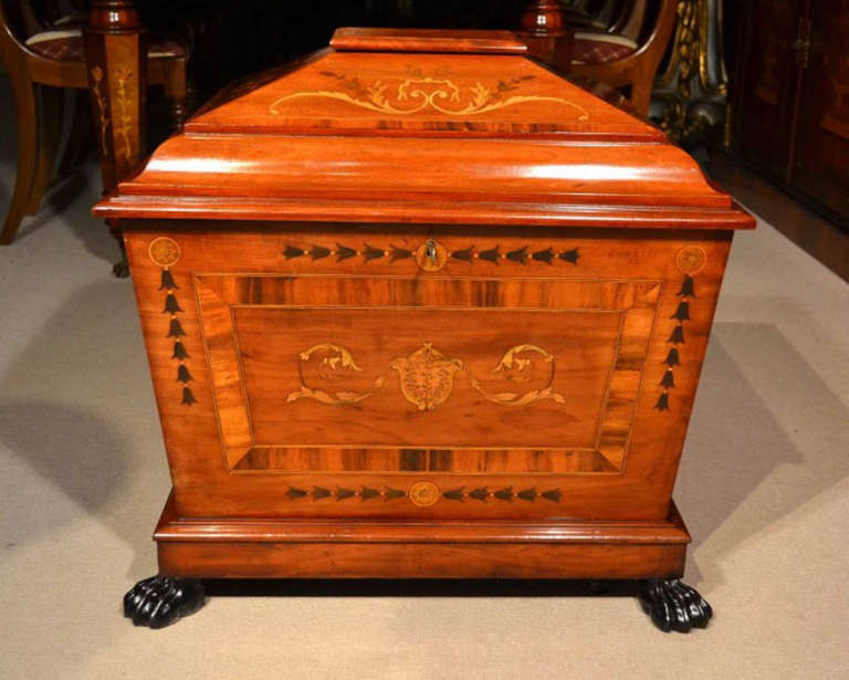 A 19th century crossbanded mahogany and marquetry sarcophagus cellarette, c.1880.

The hinged top encloses a zinc lined reservoir with provision for six bottles. The marquetry decoration comprises ribbons, bell husks and leafy scrolls. the whole