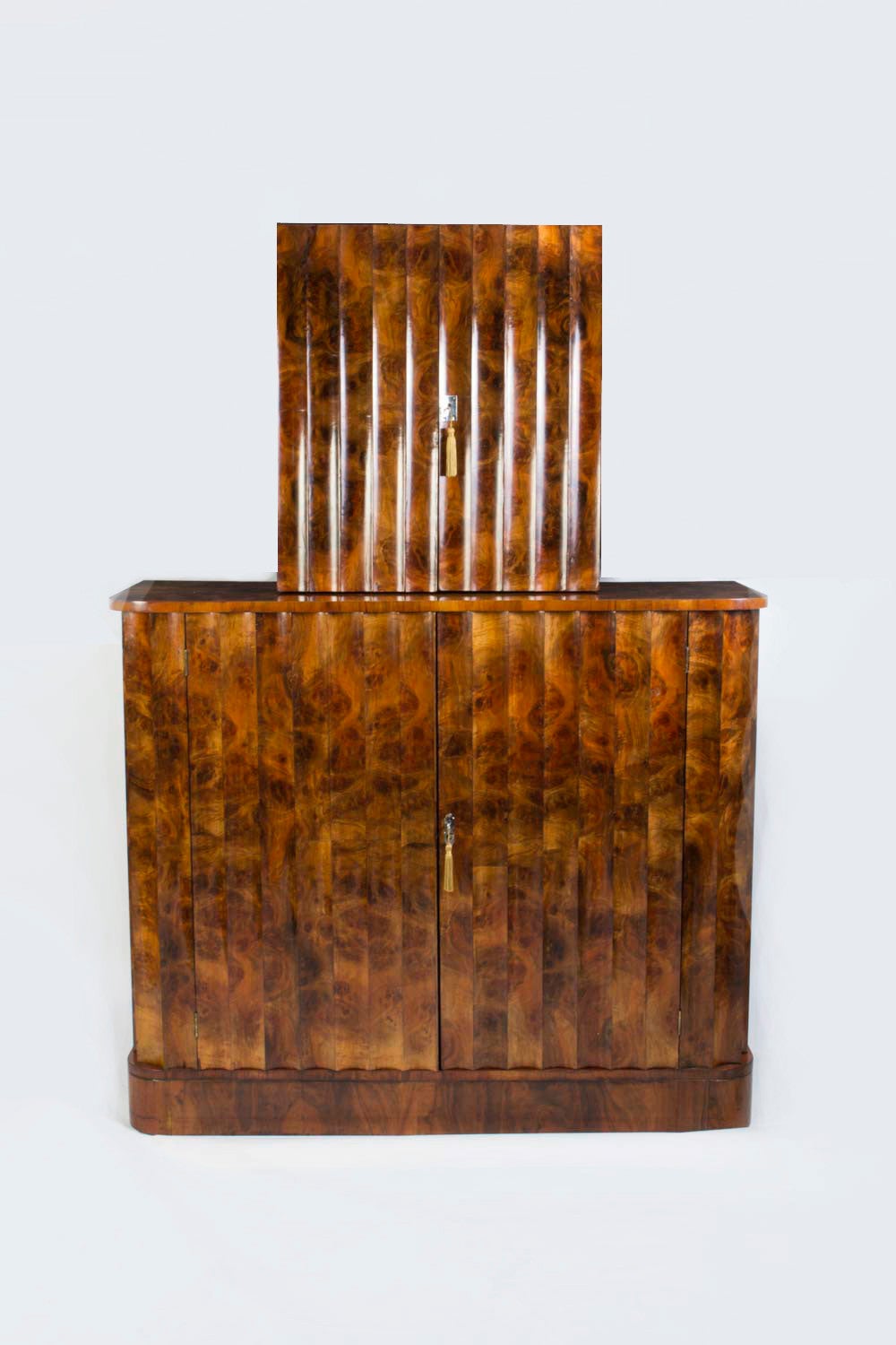 This is a very elegant antique Art Deco burr walnut cocktail cabinet circa 1920 in date. 

The cocktail cabinet is in two parts with fluted front and sides. 

The top section opens to reveal a mirrored interior with glass shelves and a pull out