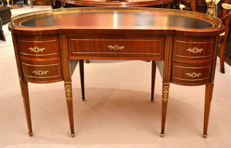This gorgeous antique kidney desk is crafted from beautiful mahogany and features a beautiful leather top that has been hand dyed and gold tooled. It has been inlaid with brass by a master craftsman, the quality of the work is breathtaking. 

The