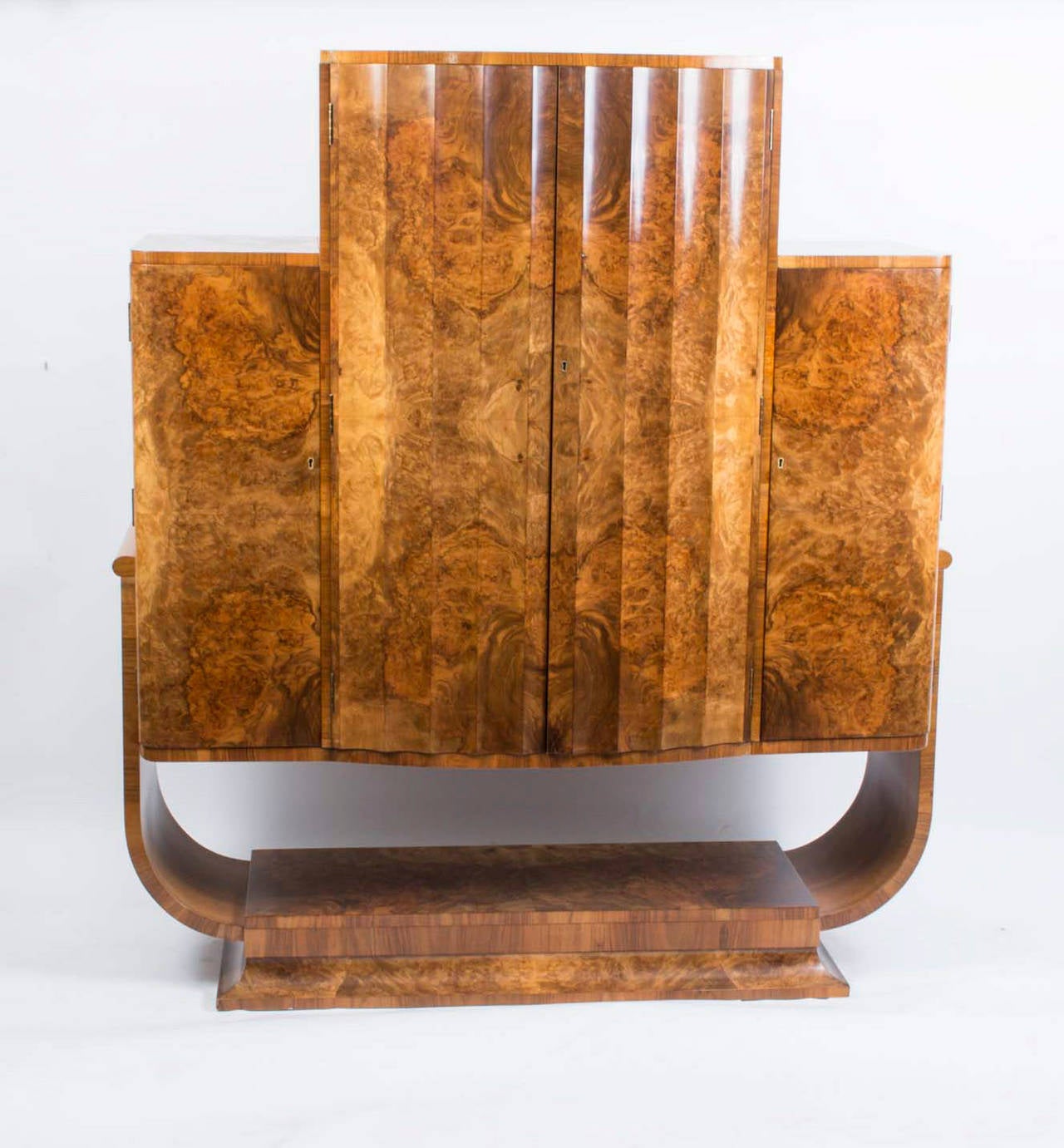 This is a very elegant antique Art Deco burr walnut cocktail cabinet circa 1920 in date. 

The cabinet rests on a lovely oval base and has a large pair of fluted doors in the middle with a smaller door on each side. 

The middle section opens to