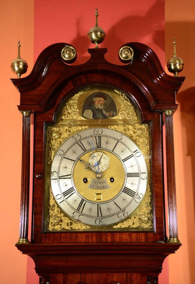 This is an antique George III inlaid flame mahogany longcase clock by John Benson of Whitehaven, Circa 1780 in date. 

The case with brass finials to the swan neck pediment supported on brass-capped columns, the arched waist door centred by inlaid