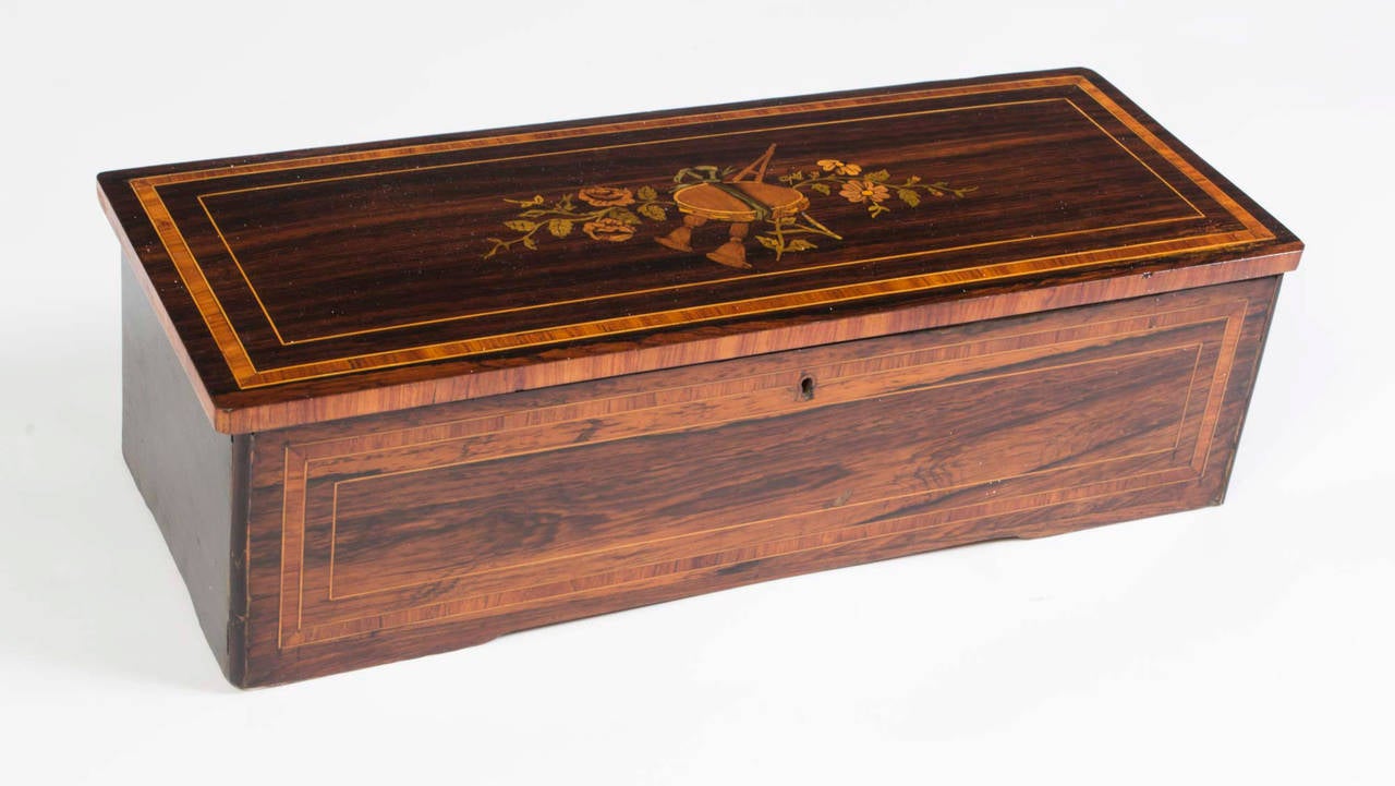 This is a lovely antique Swiss 8 airs rosewood cylinder music box, manufactured by Ducommun Girod, circa 1880. The rosewood case is inlaid and crossbanded with kingwood & boxwood, and there are lovely marquetry decorations of musical instruments