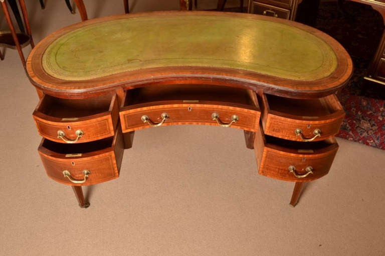This is an antique Edwardian mahogany and satinwood crossbanded kidney shaped writing table circa 1900 in date. The desk bears an enamel label for Waring & Gillow the renowned furniture makers. 

The desk has the original green gold tooled leather