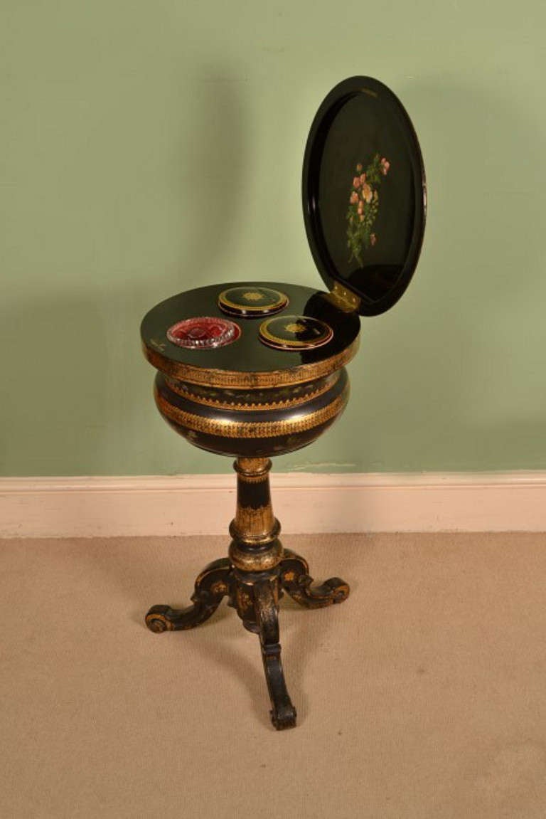 This is an antique Victorian black lacquered Papier Maché, teapoy, circa 1880 in date. It has gilded decoration and the hinged cover has hand painted floral decoration. 

The beautiful interior comprises a pair of cylindrical lidded zinc lined