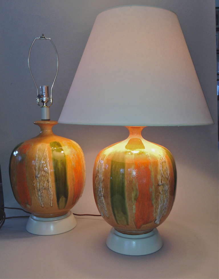 A matched pair of glazed pottery lamps, with pumpkin tan body, and gestural stripes of dark orange, green, and white. Balanced on spun metal bases, with sandy coloration on base and stem. New Chrome harp, and high quality socket. brown silk cording
