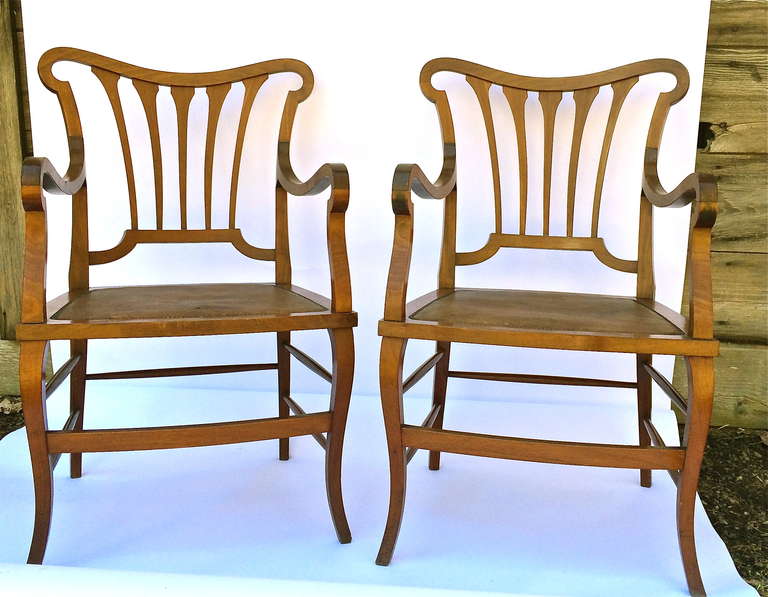 A matched pair of early 20th century Nouveau armchairs. Graceful, stunning lines and proportions, in honey colored fruitwood. Retaining the original finish, and leather inset seats. Possibly the design of Bruno Paul or Henry Van De Velde. These are