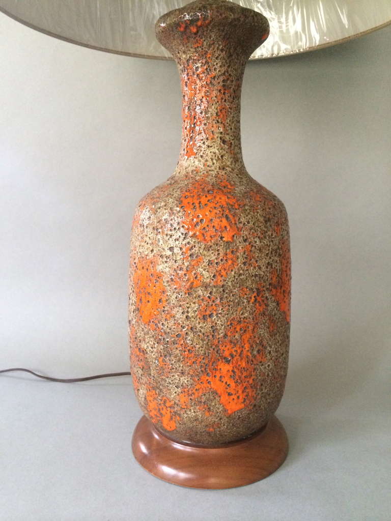 A single glazed pottery lamp, with tactile lava glazing in bright orange under semi translucent burnt white overglazing. Classical bottle form, with original wooden pedestal and brass hardware. Shade pictured is for display purposes only.