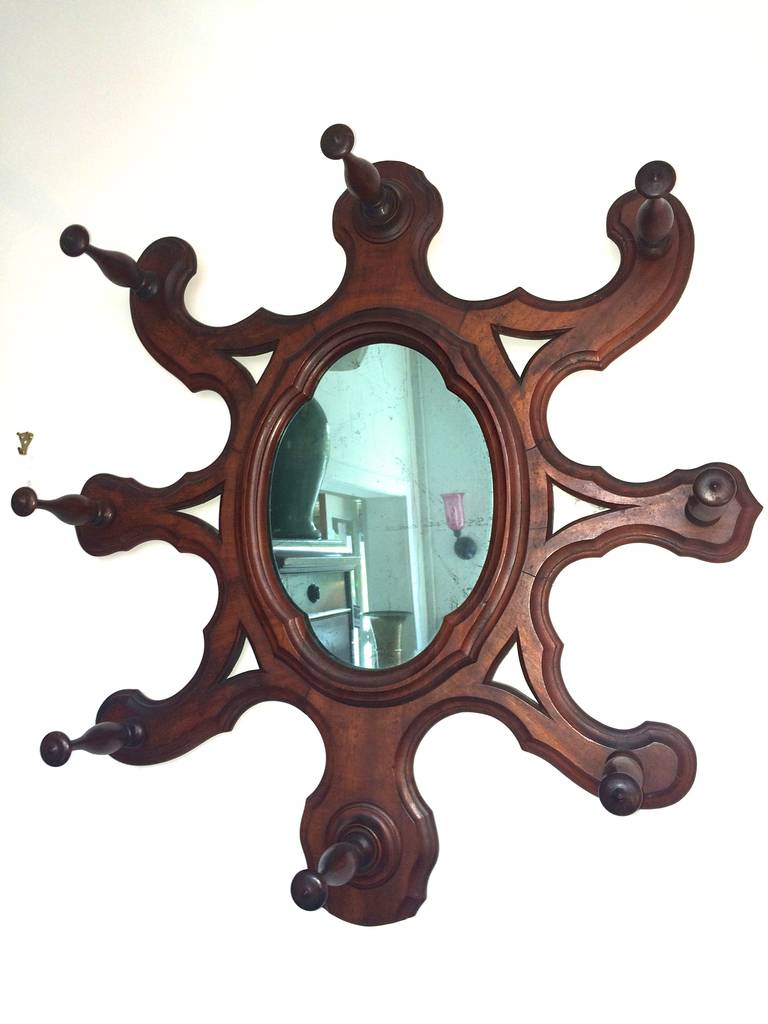 Mahogany wall mounting hat rack with finely turned pegs in a starburst pattern around oval looking glass. A breathtaking version of a classic design in the Gothic taste.