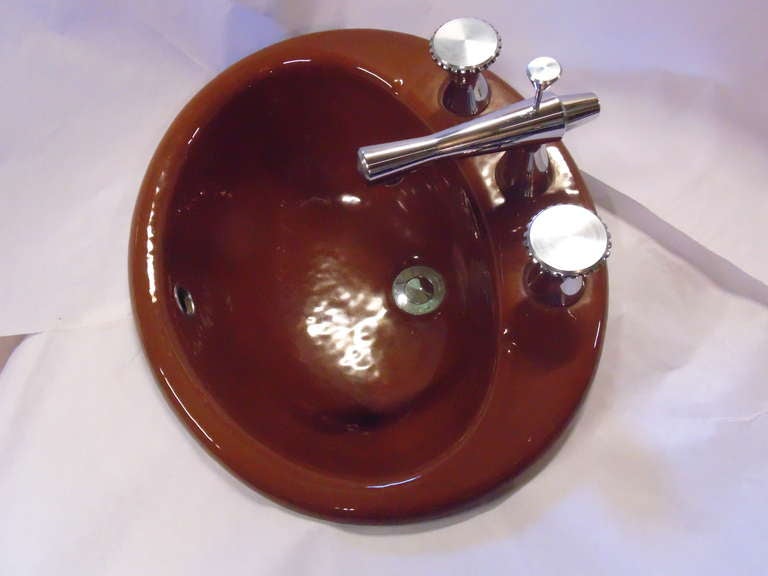 A matched pair of vitreous porcelain sinks, in chocolate brown, with matching machined chrome hardware. retaining their original faucets, with chromed finish.