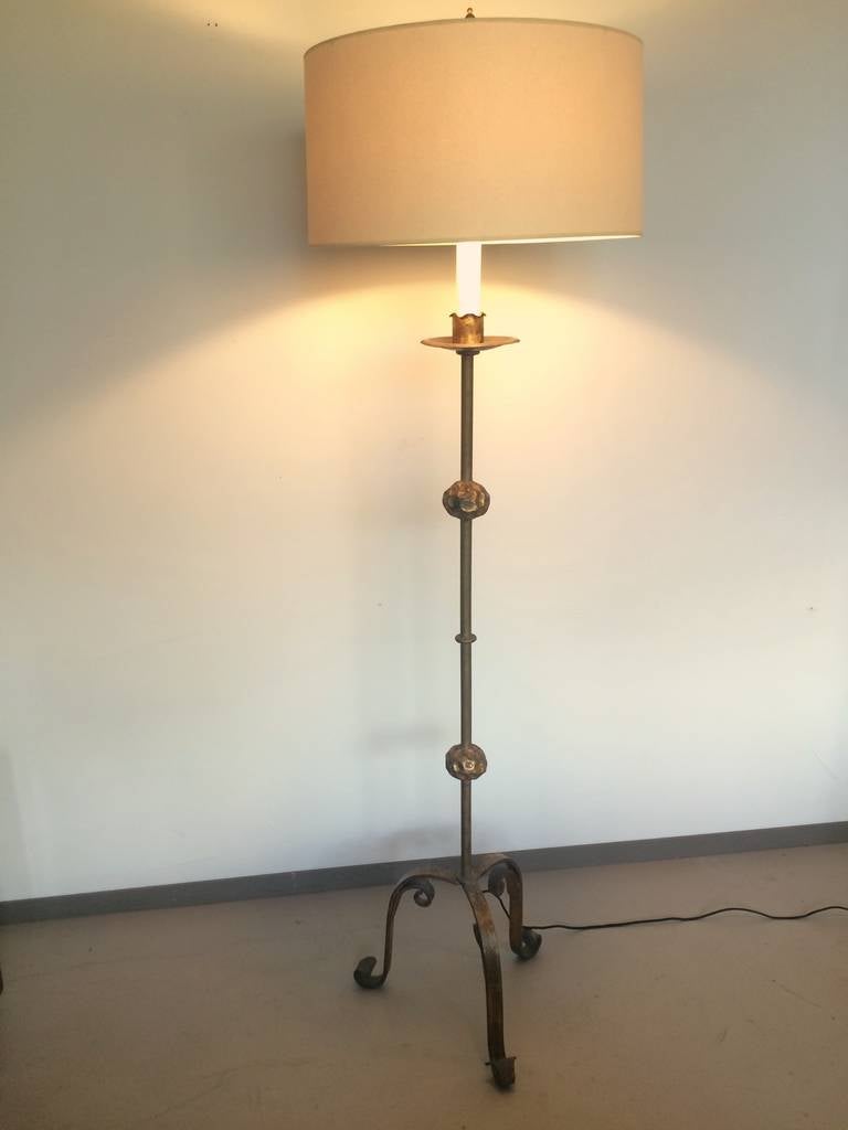 A single wrought iron standing lamp with gilt surface. A simple, elegant design with finely wrought details and a single candle stem supporting a two light cluster. Refurbished and rewired with black silk cording.