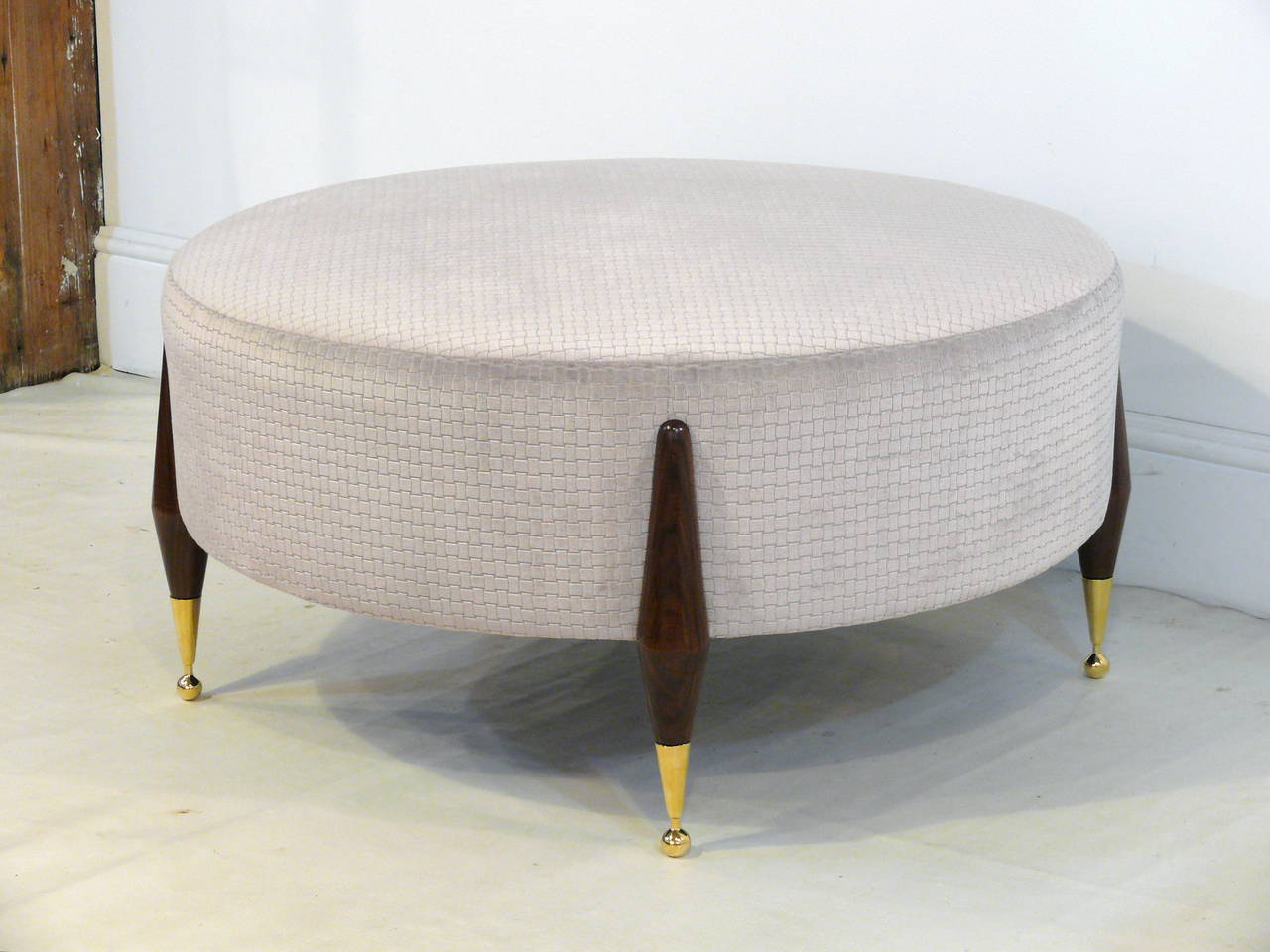 Imperial ball foot ottoman or coffee table designed by Irwin Feld Design for CF Modern. This versatile ottoman or coffee table features four sculptural walnut legs and beautiful brass ball foot sabots holding a plush custom round cushion (shown here