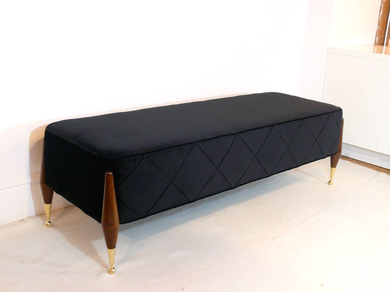 Imperial ball foot bench designed by Irwin Feld Design for CF Modern. This bench features four corner sculptural walnut legs and beautiful brass ball foot sabots holding a plush custom rectangular cushion (shown here in a black velvet). Available