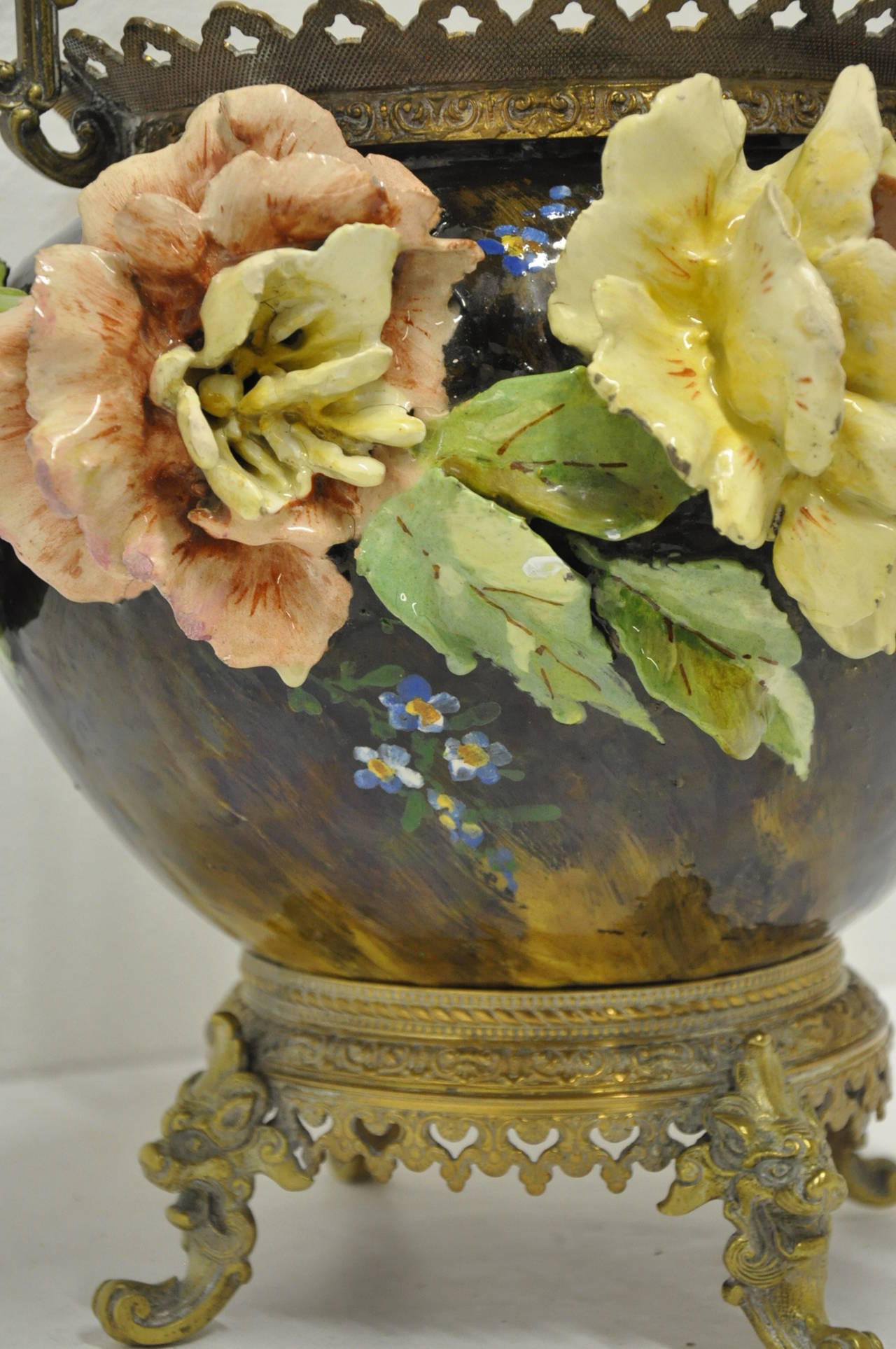 19th century barbotine majolica cache-pot  featuring relief motifs with painted flowers and leaves. The vase sits on a bronze base with bronze handles on top (circa: 1860)