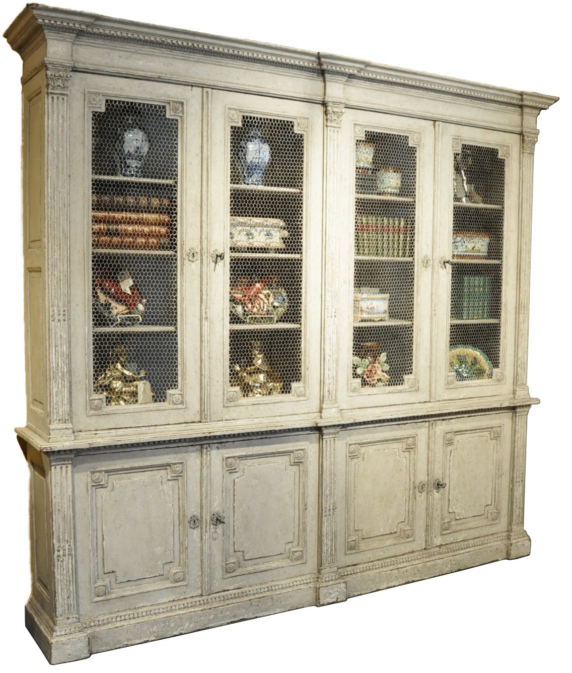 Elegant mid-19th century Louis XVI painted bookcase featuring two chicken wire double doors on top with plenty of shelving for display, circa 1840. On the bottom, there is a pair of carved doors with shelving for storage. The beautiful painted