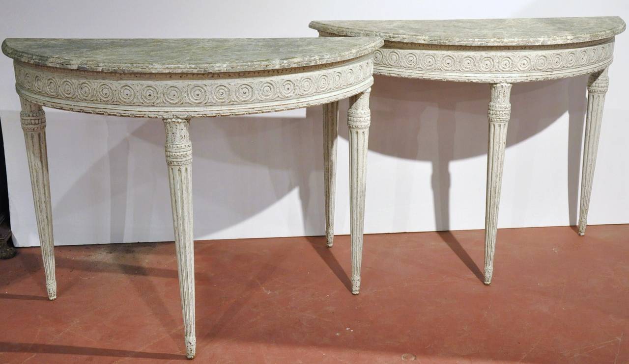 Pair of antique demilune consoles from France, circa 1880; each table features three tapered and fluted legs with delicate carved decor on the curved apron. The top has a faux marble finish. Excellent condition with rich old painted