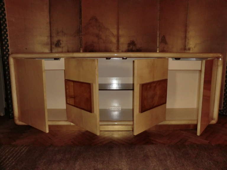 Credenza made in parchment with a glossy layer of polyester coat with beautiful vintage patina,  some crack on the side and top see images attached , brass decorative panels, smoke glass top, two drawers, gold leaves finishing base