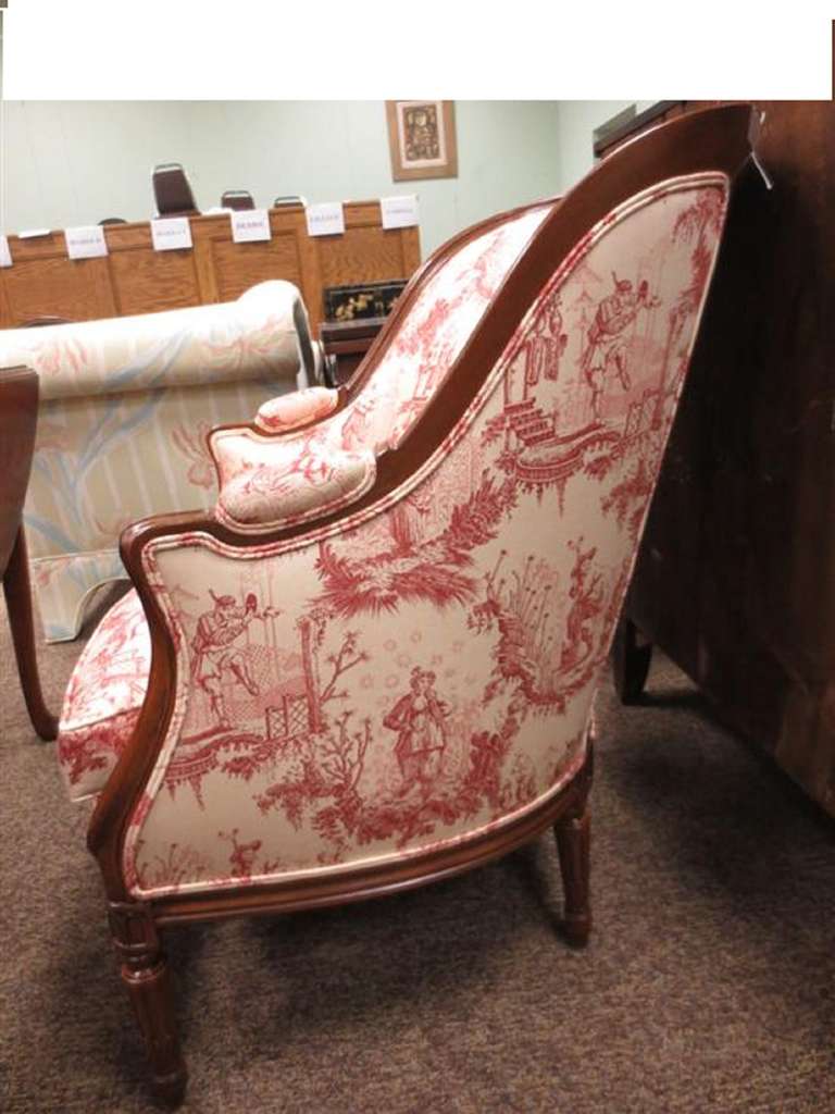 20th century Louis XVI style upholstered carved mahogany bergere or armchair, scrolling armrest with carved stiles, on tapered fluted legs. Down cushion.