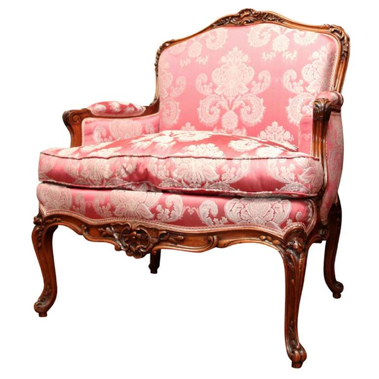 20th century upholstered Louis XV style walnut bergere or armchair. The padded back above a loose cushion seat, raised on foliate carved legs.