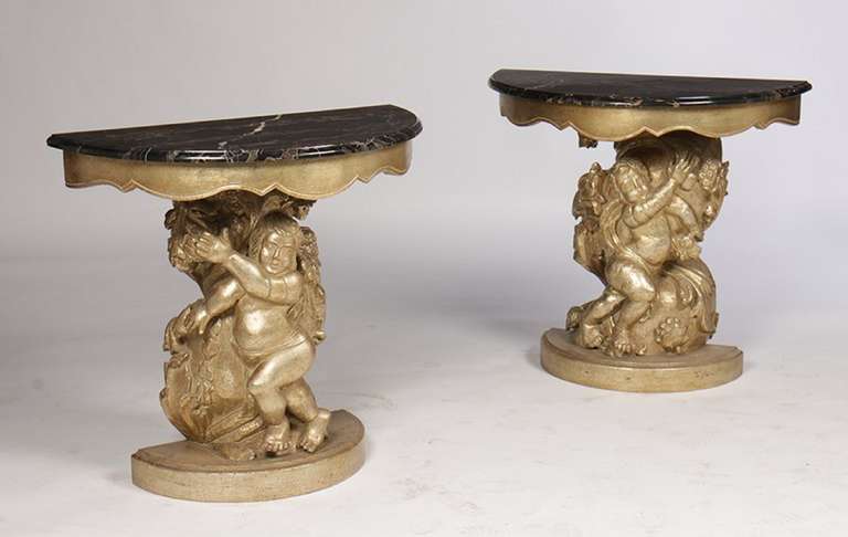 20th century Italian pair of giltwood and silver gilt carved figural consoles with decorative marble tops. Supported on putti and foliate decorated pedestal and raised on plinth base.