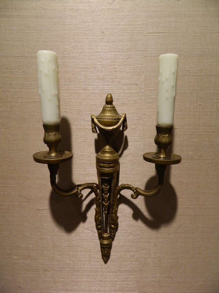 19th century Louis XVI set of three bronze wall sconces decorated with urns and garlands.  Original patina.  US wired for electricity