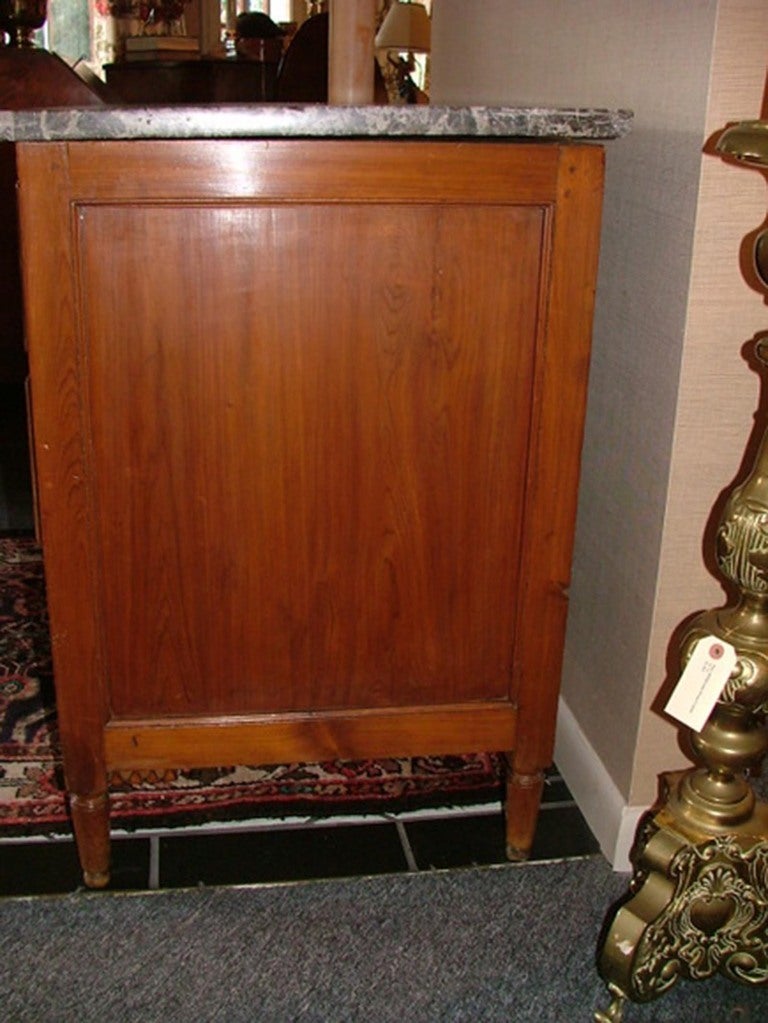 19th century Louis XVI style Provincial fruitwood and marble-top commode or chest of drawers, the rectangular variegated charcoal marble top above a case fitted with three long drawers, all with shaped panels and flanked to either side by