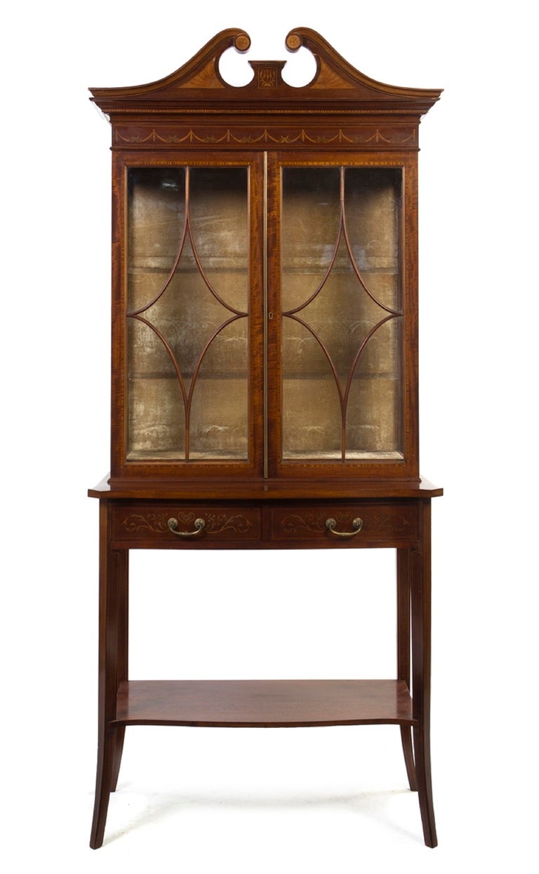 19th century George III style mahogany, satinwood and marquetry bookcase on stand, having a broken arch pediment with fan inlays above the frieze inlaid with continuous swags over two glazed doors, the base set with two drawers, raised on slightly