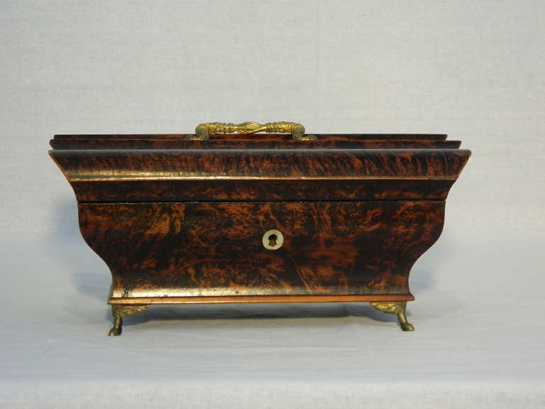 A French Early 19th Century Exotic Wood Bombe Form Brass Footed Box the serpentine form top with a brass handle above a conforming case of bombe form, having an ivory escutcheon and raised on small brass feet, the interior lined in silk
