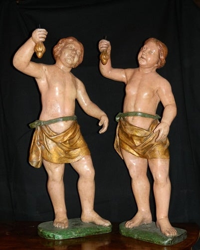 Pair of Italian painted papier mâché figural torcheres Piedmont. Each curly haired youth with pleasant expression, clad in loose drapery holding aloft a candle cup standing contra posto on a rectangular base, 18th century.