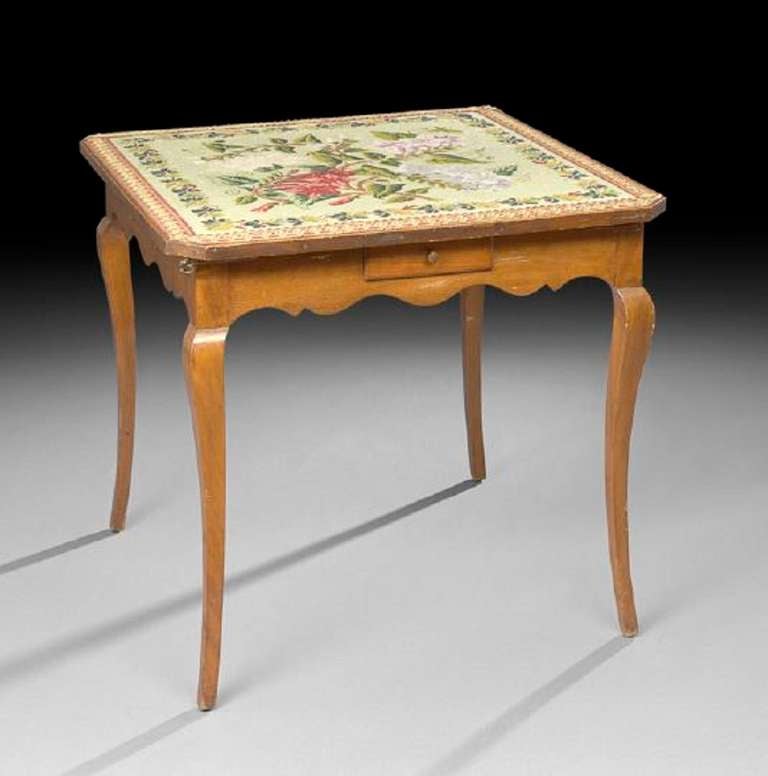19th century French Provincial fruitwood games table, the canted square top with an inset floral needlepoint panel, above a scalloped frieze fitted with corner pull-out slides and a small drawer to each side, raised on cabriole legs. Measures: H