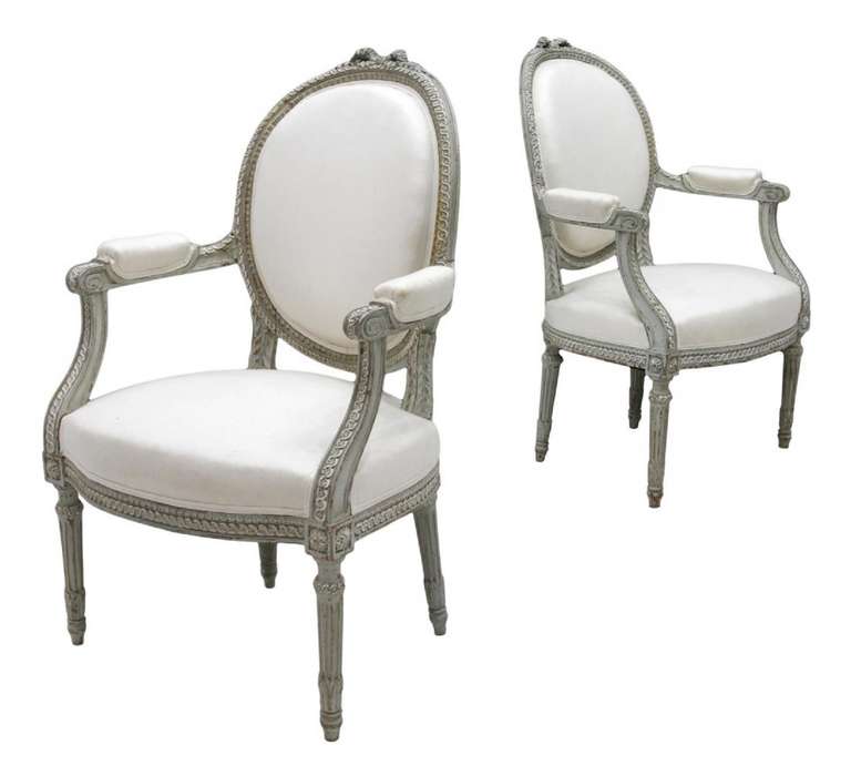Late 19th Century Pair of French Louis XVI-style fauteuil or armchairs, a carved ribbon crest over the medallion form back, incurvate padded arms rising on tapered ribbed legs.