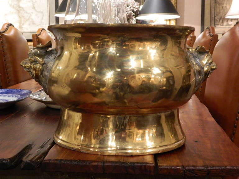 Asian-style large brass jardinière. The circular body rests on a high pedestal foot and applied with a pair of leonine masks below the flared rim. Diameter of opening is 10.5